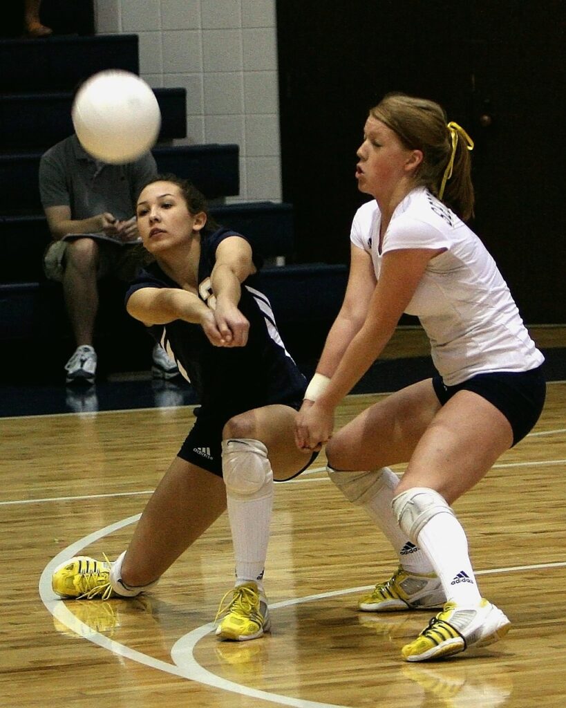 Two women playing volleyball in a gymnasium.