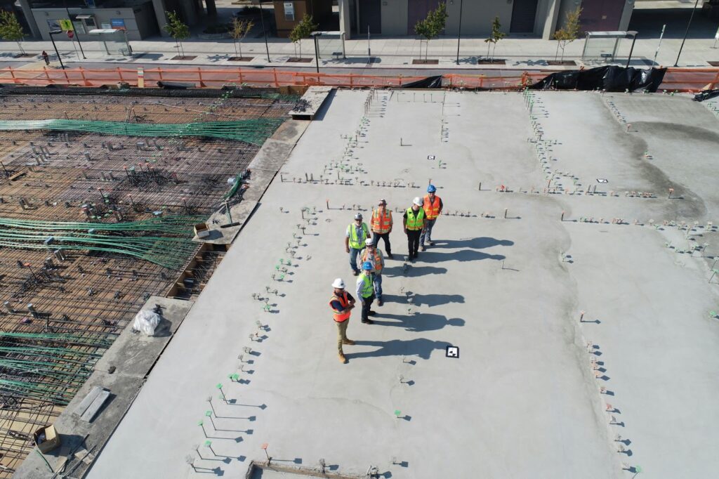 Several construction workers stand on a building’s concrete foundation.