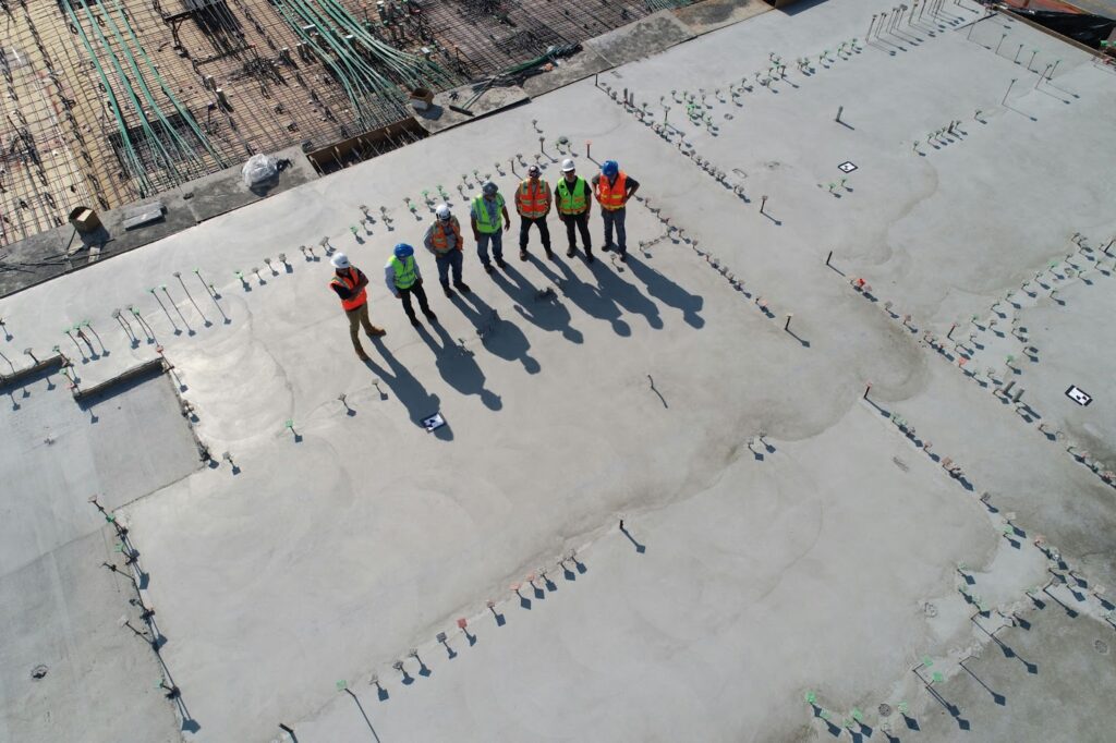 Several construction workers stand on a building’s concrete foundation.