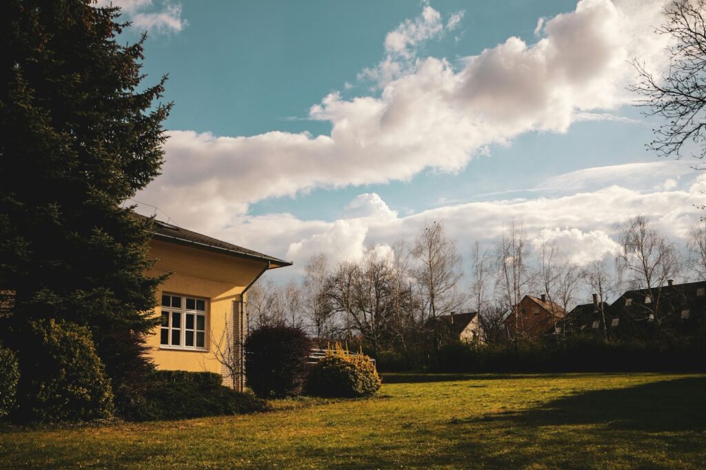 An out building with a tree and bushes on a large lawn