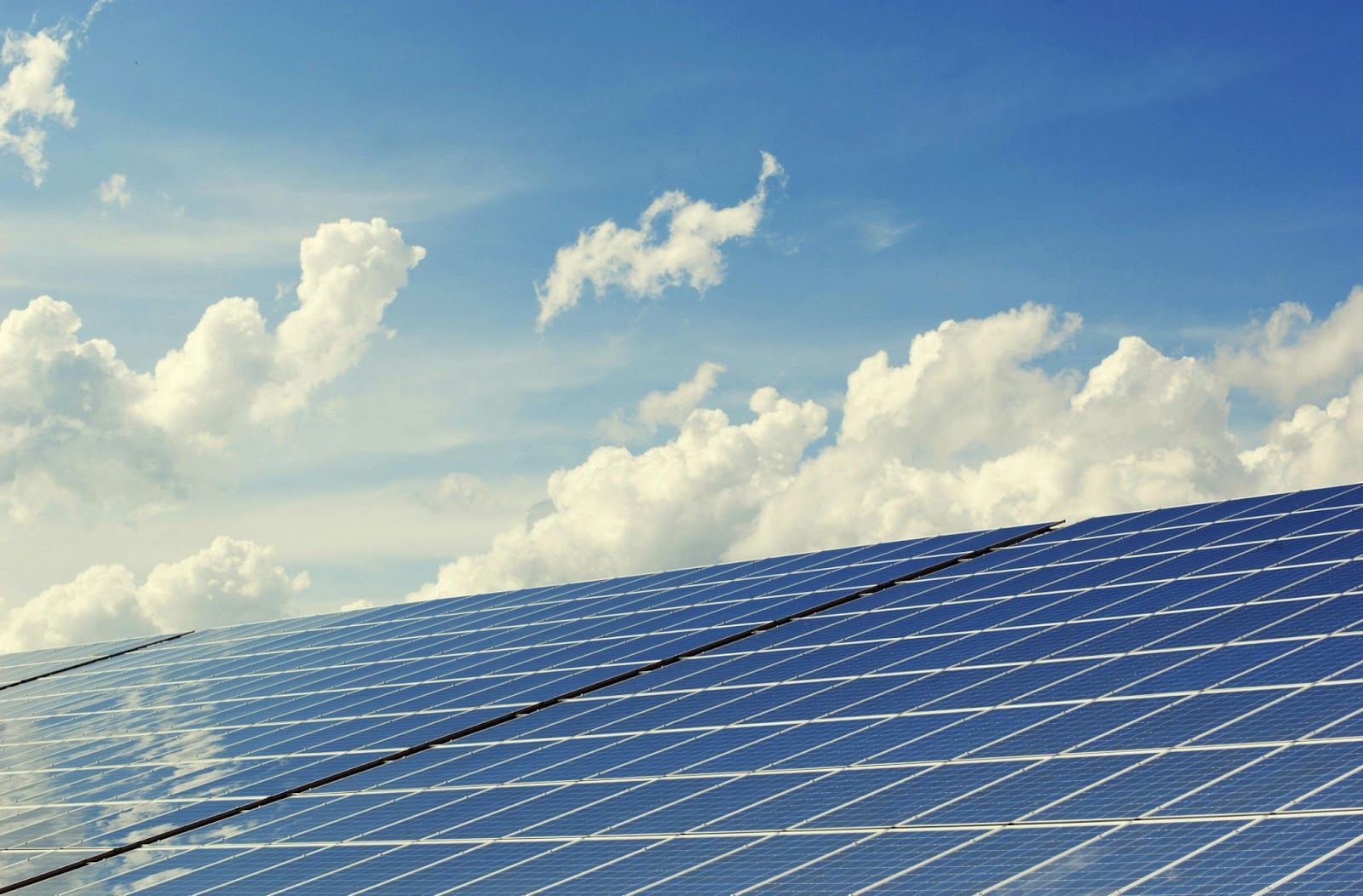 Up close image of solar panels installed on a metal roof with clouds in the sky.