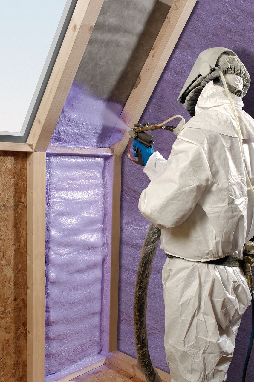 A person wearing a protective suit, goggles, and a face mask while carrying a foam insulating a room.