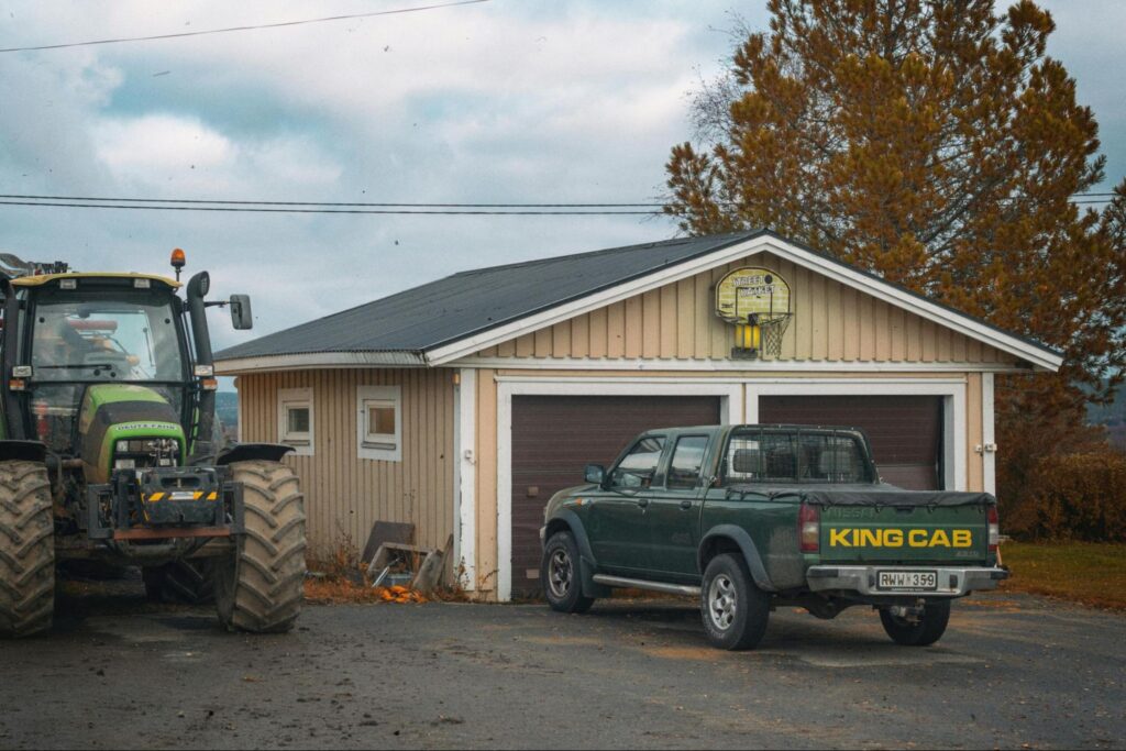 A pickup truck and tractor parked outside of a farm equipment shelter.