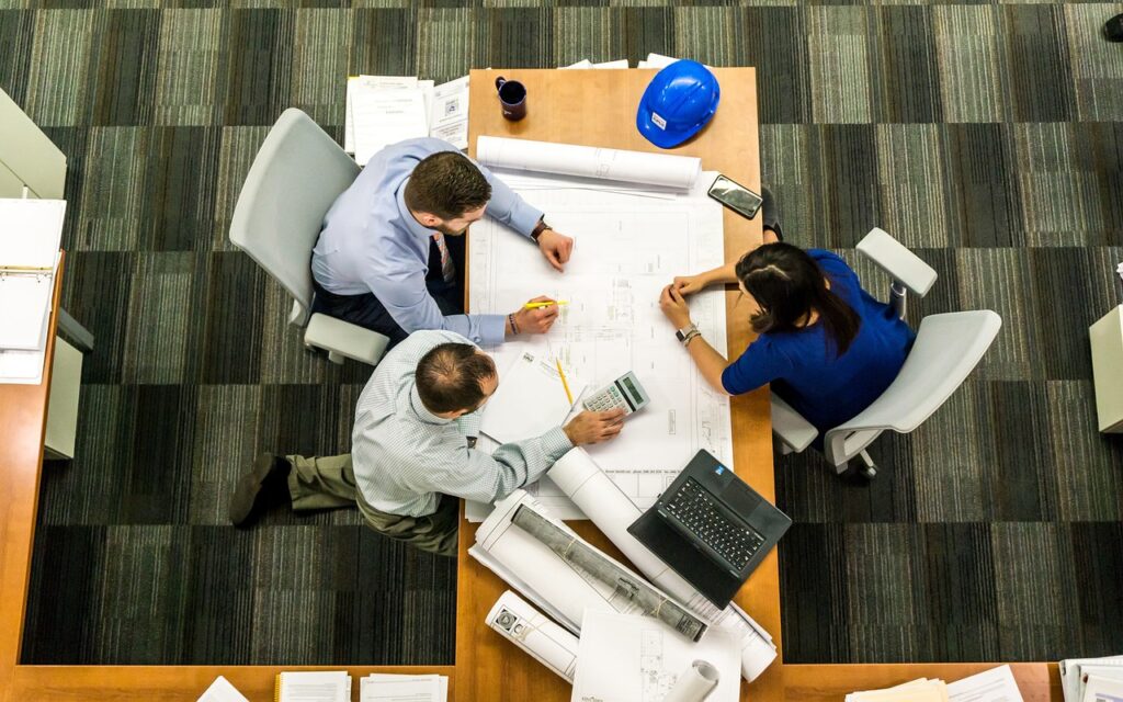 Three people sit at a table discussing a construction project.